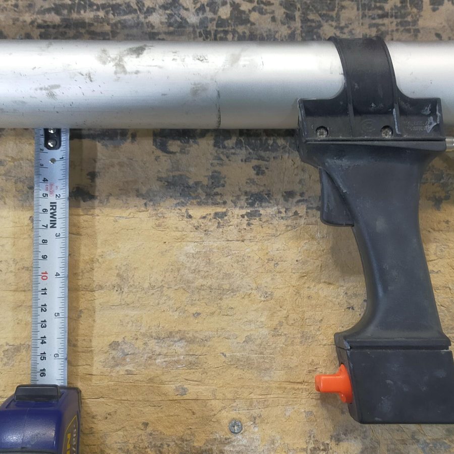 A pneumatic caulking gun on a workbench with a tape measure under its barrel